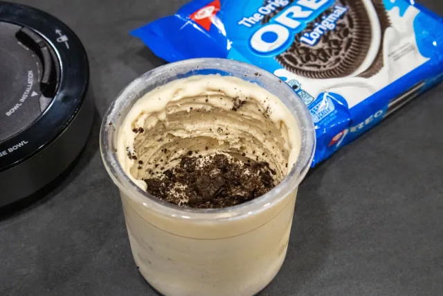 High protein Oreo McFlurry in a clear cup with crushed cookie pieces on top, beside an Oreo package and blender.