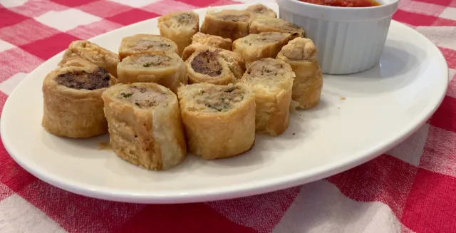 Golden-brown air fryer sausage rolls arranged on a white plate with dipping sauce, on a red and white checkered tablecloth.