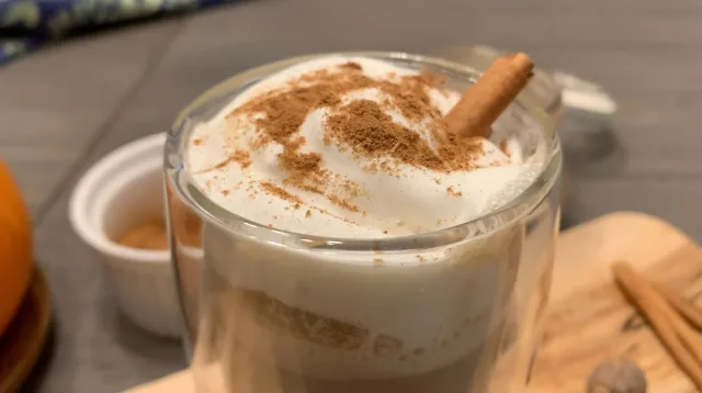 Homemade pumpkin spice latte topped with whipped cream and cinnamon in a glass mug with cinnamon stick.