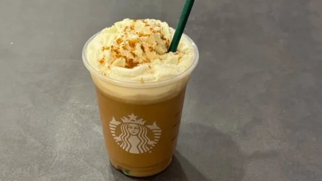 Iced Pumpkin Spice Latte topped with whipped cream and cinnamon crumble in a Starbucks cup with green straw.