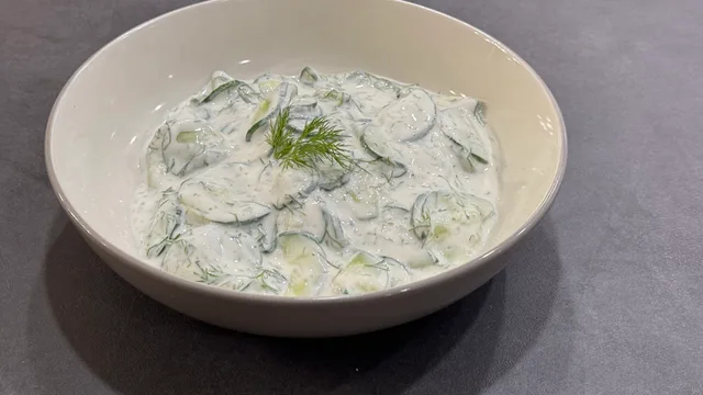 Classic German Gurkensalat in a white bowl with sliced cucumbers in creamy dressing, garnished with fresh dill.