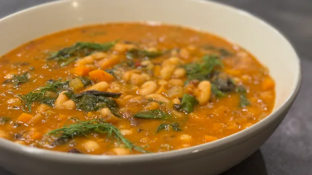 White bean harissa stew with chickpeas and fresh herbs in a white bowl.