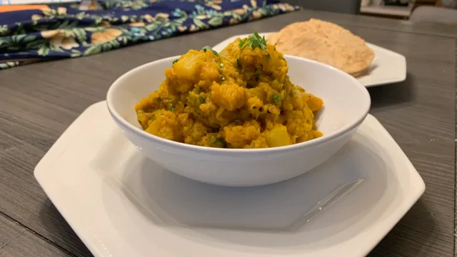 Aloo Kohra Sabji curry served in a white bowl, golden turmeric-spiced potatoes and pumpkin with fresh cilantro garnish.