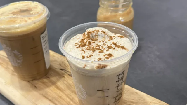 Pumpkin cream cold brew in a clear cup topped with cinnamon, alongside jars of pumpkin cream and coffee.