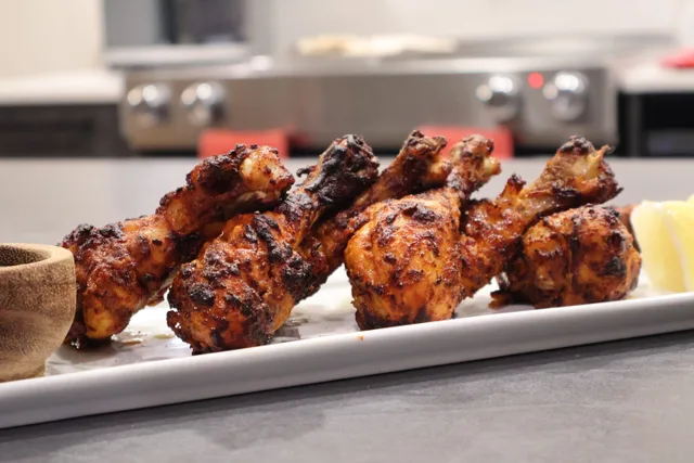 Cooked tandoori chicken skewers on a white plate with lemon wedge and sauce in a kitchen setting.