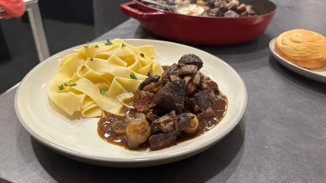 Beef Bourguignon served on a white plate with buttered egg noodles and pearl onions in rich brown sauce.
