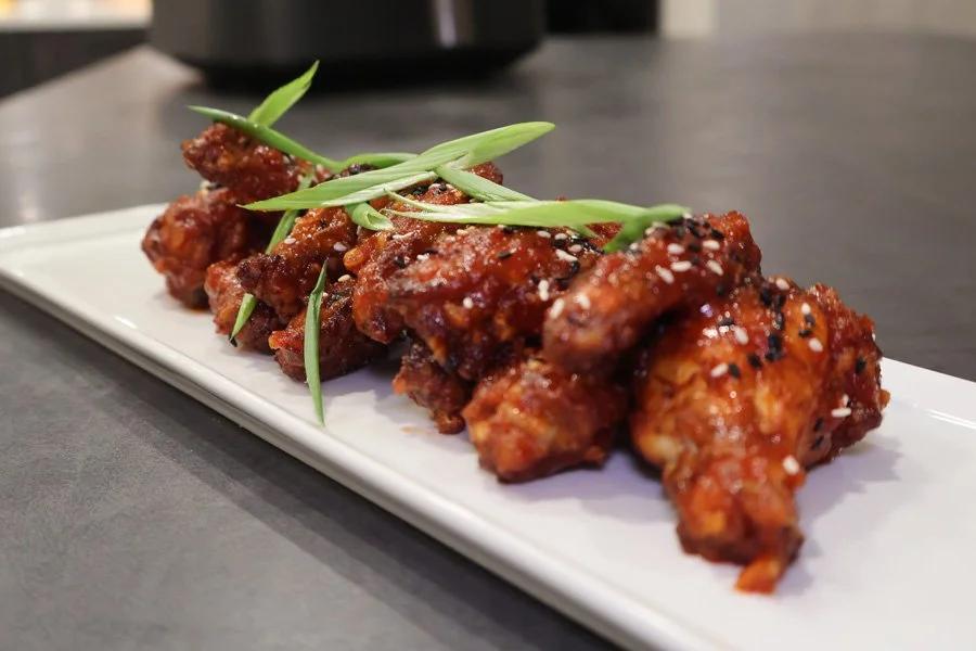 Crispy Korean fried chicken wings glazed with sauce, sesame seeds, and green onion strips on a white plate.