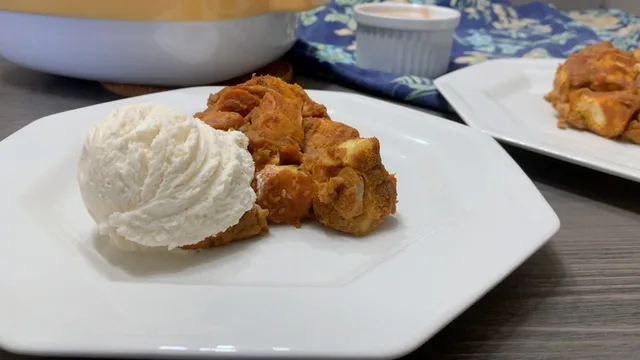 Warm pumpkin banana bread pudding chunks topped with a scoop of vanilla ice cream on a white plate.