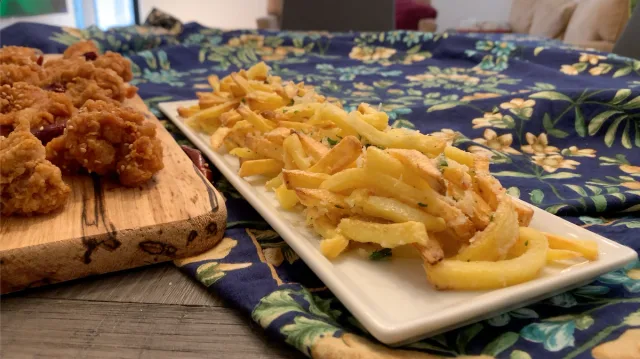 Crispy air fryer garlic parmesan fries on a white plate next to fried chicken on a wooden board.