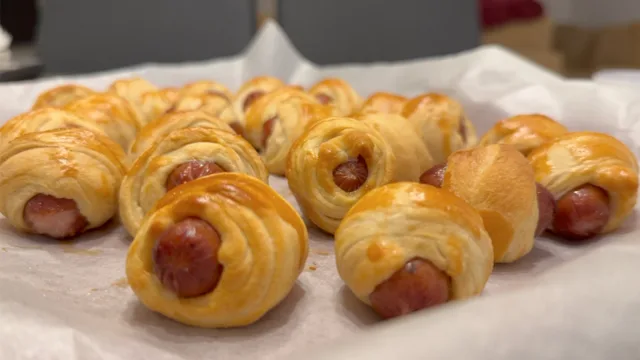 Golden baked crescent roll pigs in a blanket with hot dogs wrapped in flaky pastry on parchment paper.