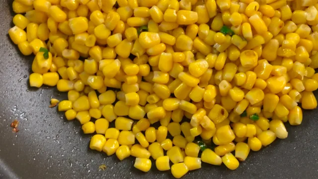 Golden corn kernels cooking in a dark pan for masala corn fry