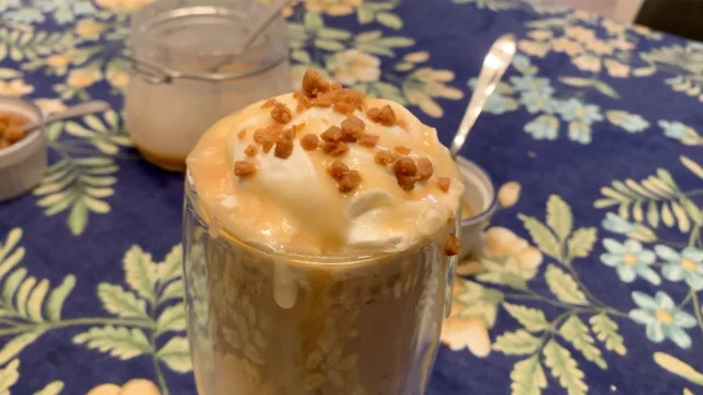 Caramel Ribbon Crunch Frappuccino topped with whipped cream and toffee bits in a tall glass.