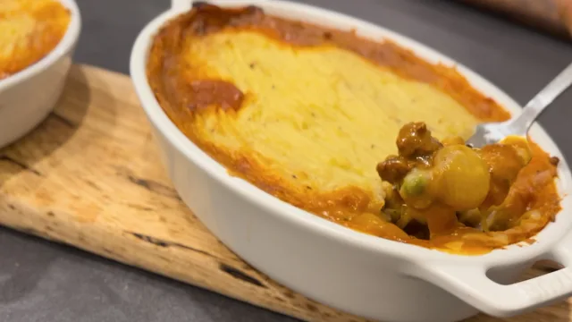 Golden-topped shepherd's pie in a white ceramic dish with visible meat and vegetable filling on the side.