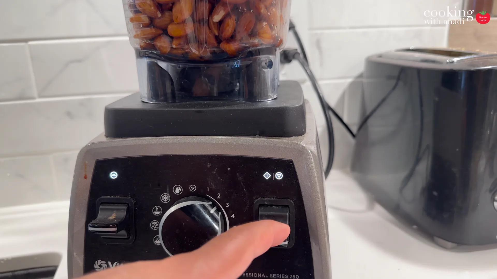 Roasted hazelnuts in the Vitamix jug as a hand turns the dial on