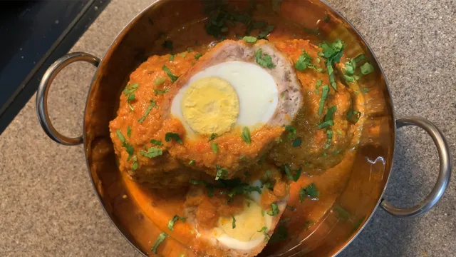 Chicken Nargisi Kofta Curry in a copper pot, topped with sliced hard-boiled eggs and fresh cilantro garnish.