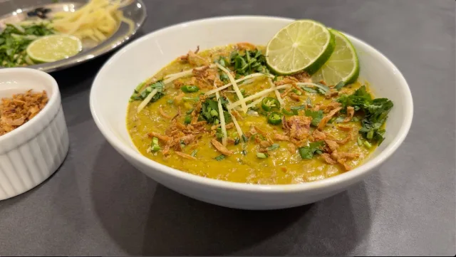 Bowl of Pakistani lamb haleem topped with crispy fried onions, fresh cilantro, ginger, and lime slices.