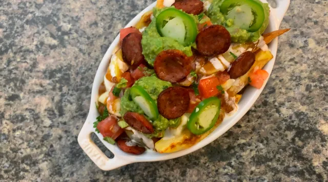 Mexican fusion poutine topped with chorizo, jalapeños, bell peppers, and cheese on a white oval plate.