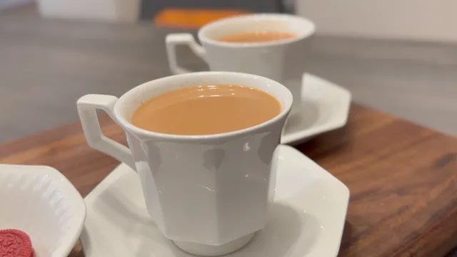 Two cups of Indian ginger tea with creamy tan color served in white mugs on wooden surface.