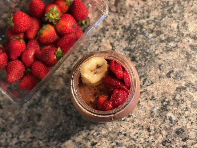 Chocolate banana strawberry overnight oats in a glass jar topped with sliced banana, beside fresh strawberries.