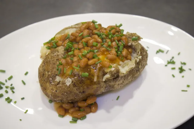 Baked potato topped with baked beans and fresh chives on a white plate