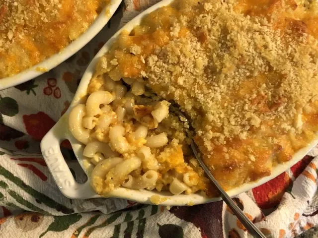 Creamy mac and cheese with golden breadcrumb topping in white baking dishes with spoon.