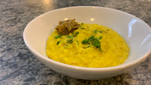 Bowl of golden yellow khichdi garnished with fresh cilantro and topped with a dollop of ghee on granite countertop.