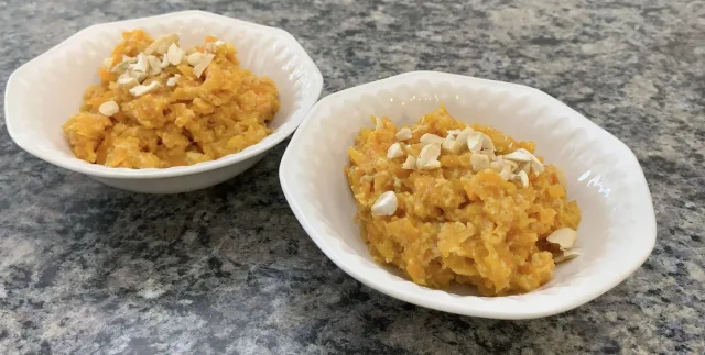 Two bowls of gajar ka halwa topped with sliced almonds on a gray granite countertop.