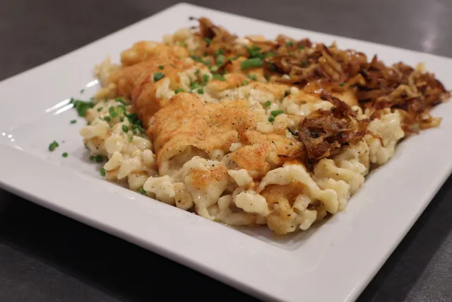 Käsespätzle served on a white plate with crispy fried onions, melted cheese, and fresh chives.