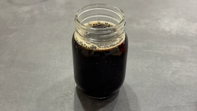Dark gingerbread syrup in a glass jar with foam on top, ready to use.