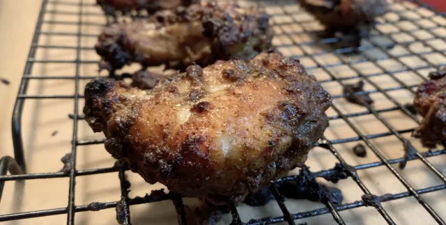 Crispy air fryer jerk chicken wings cooling on a wire rack, golden-brown with caramelized seasoning.