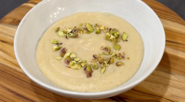 Creamy semolina pudding garnished with chopped pistachios in a white bowl on a wooden surface.