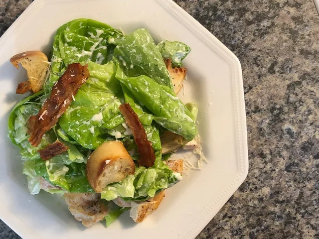 Grilled chicken Caesar salad with crispy croutons, bacon, and fresh romaine lettuce on a white plate.