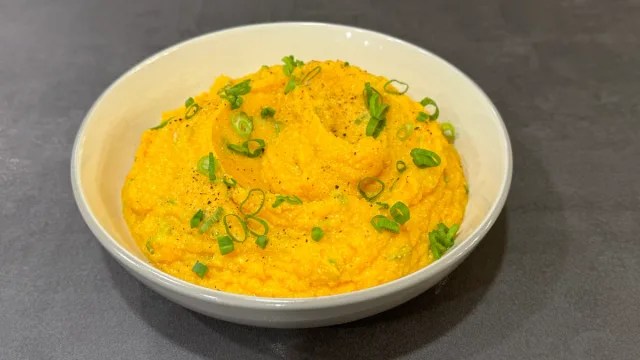 Creamy golden mashed sweet potatoes topped with black pepper and sliced green onions in a white bowl.