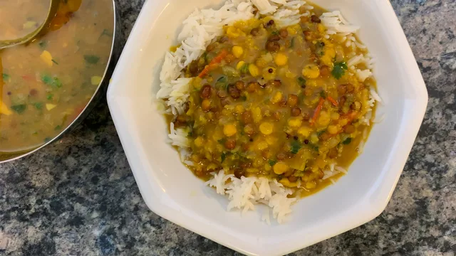 Dal Tadka served over white rice in a bowl, topped with a golden curry sauce studded with lentils and vegetables.
