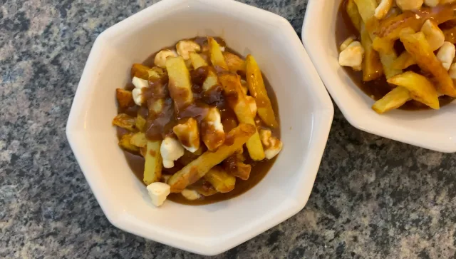 Two white bowls of poutine with golden fries, gravy, and melted cheese curds on gray countertop.