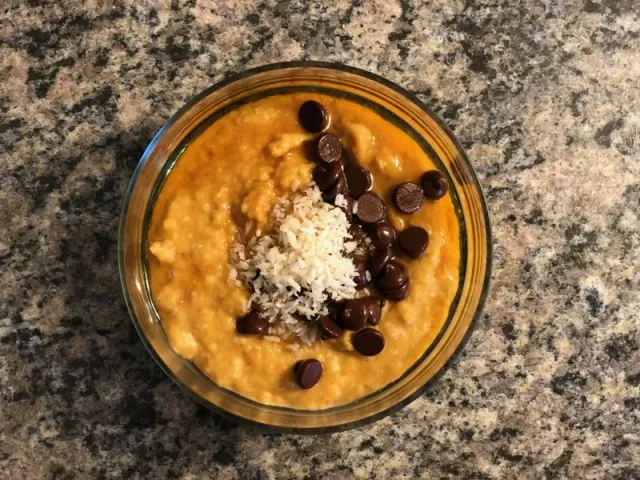 Pumpkin puree oatmeal bowl topped with chocolate chips and shredded coconut in a glass bowl.