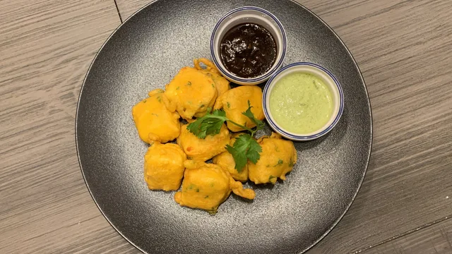 Crispy golden paneer pakora served on a gray plate with cilantro garnish and two dipping sauces.