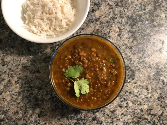 Creamy masoor dal in a glass bowl garnished with cilantro, served with white rice in the background.