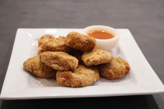 Golden-brown crunchy air fryer chicken nuggets on a white plate with a small bowl of dipping sauce.