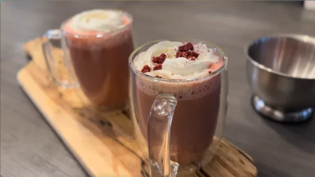 Two red velvet lattes topped with whipped cream and dried cranberries on a wooden serving board.