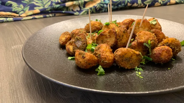 Golden-brown air fried baby potatoes on a dark plate, garnished with fresh cilantro and wooden picks.
