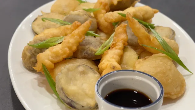 Golden crispy tempura shrimp and vegetables on a white plate with green onion garnish and soy dipping sauce.