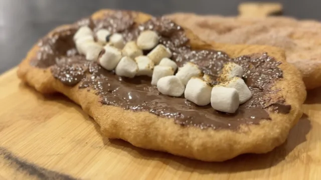 Homemade Canadian Beavertails topped with chocolate spread and mini marshmallows on a wooden board.