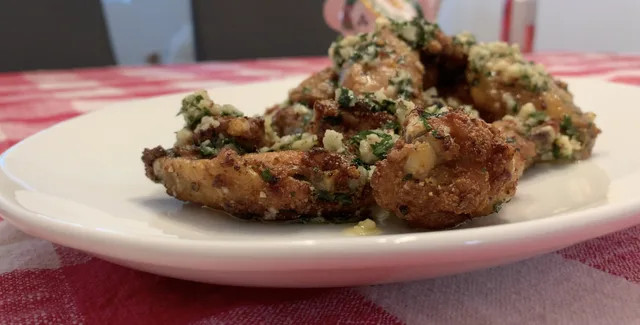 Crispy air fryer garlic parmesan chicken wings topped with fresh herbs on a white plate.