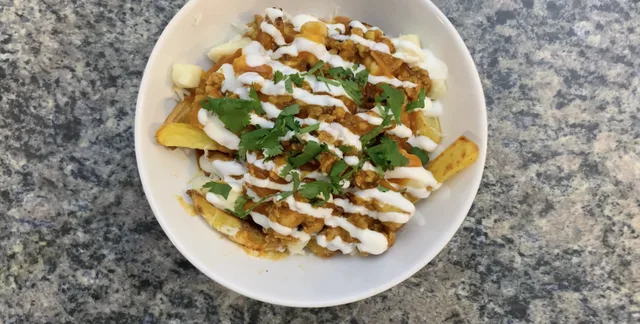 Indian Fusion Aloo Keema Poutine with crispy fries, meat sauce, creamy topping, cilantro and green onions on white plate.