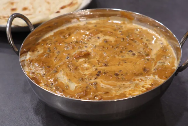 Creamy dal makhani curry in a stainless steel serving bowl with naan bread in the background.