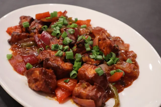 Air fryer chilli paneer served on a white plate, garnished with green onions and red peppers in a glossy sauce.