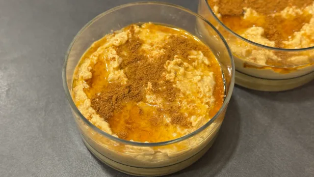 Two glass cups of creamy pumpkin rice pudding topped with cinnamon on gray surface.