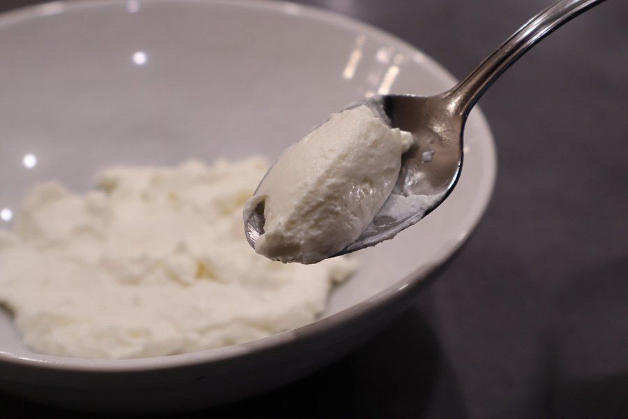 Spoon holding creamy hung curd above a bowl of strained yogurt.