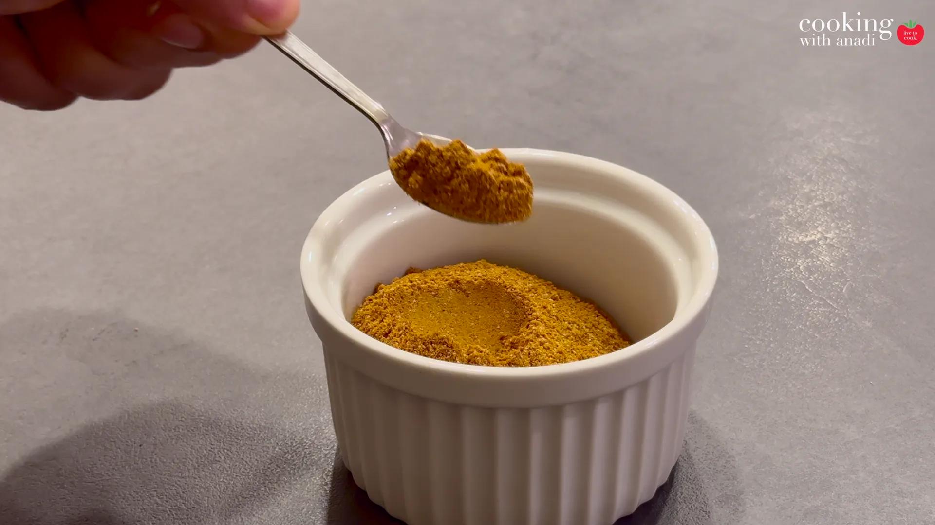 A spoon lifting fine orange curry powder from a small white ramekin
